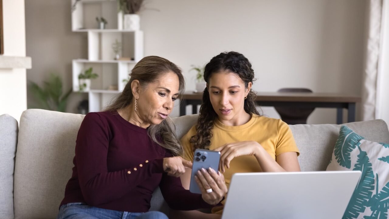 Two women looking at a phone sitting down on couch