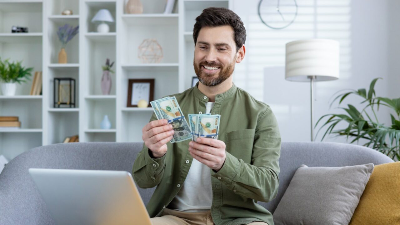 Guy looking at laptop counting money and tracking revenue
