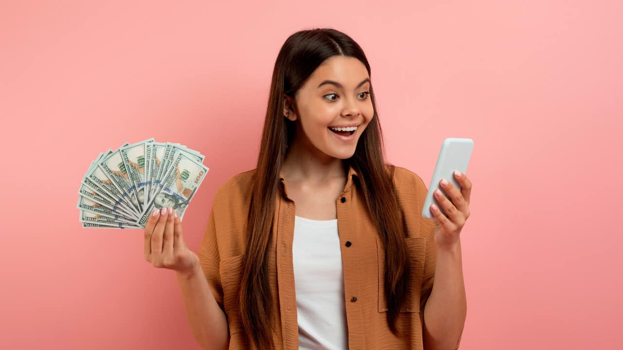 Girl smiling holding money and phone celebrating online business success