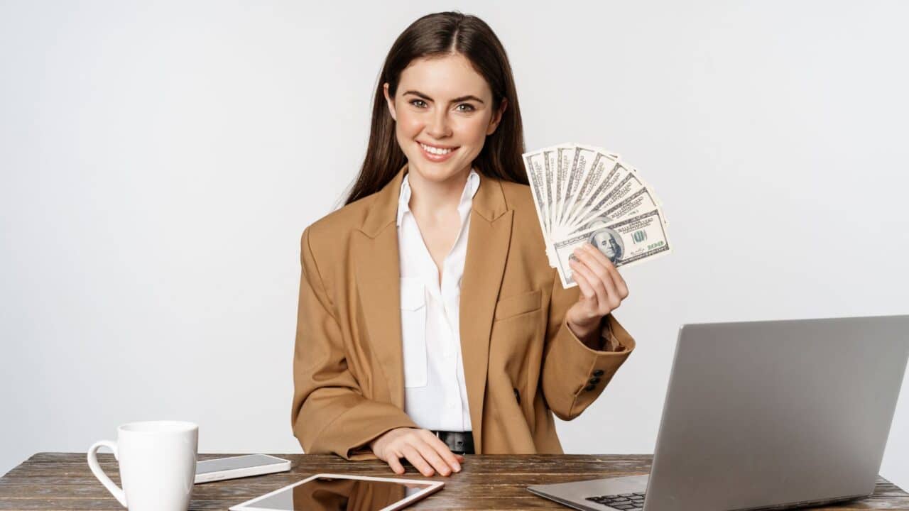 1_businesswoman_at_desk_holding_cash_profit_success