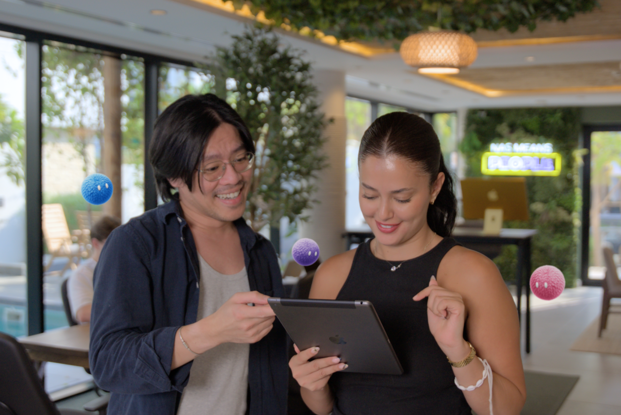 Two colleagues reviewing a shared tablet with Nas AI agents nearby.
